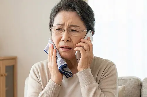 口元を抑えて電話をする初老の女性